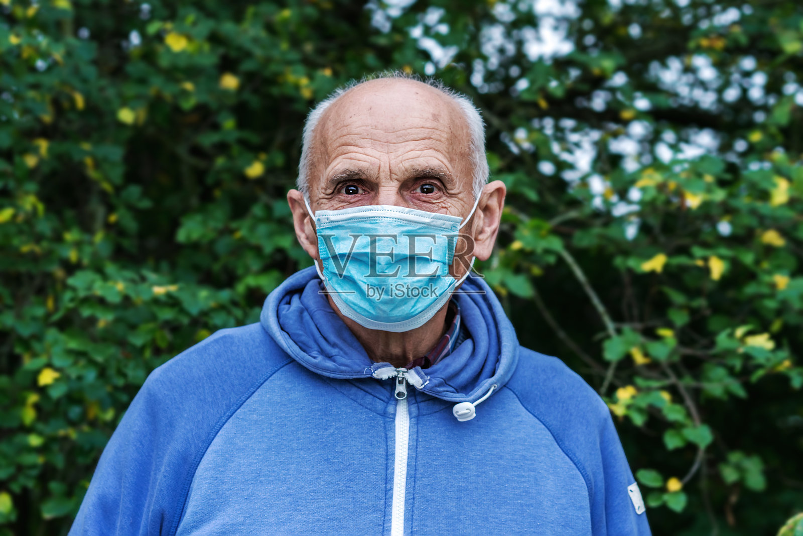 外面的老人肖像戴着面具,站在花园里照片摄影图片