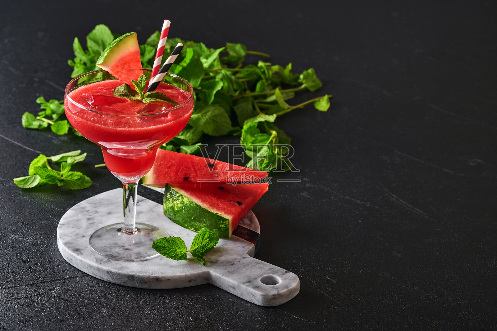 一杯西瓜加薄荷和冰的玛格丽塔鸡尾酒。黑色桌子上的玻璃杯里装着夏日清凉饮料。夏季健康饮食的概念照片摄影图片