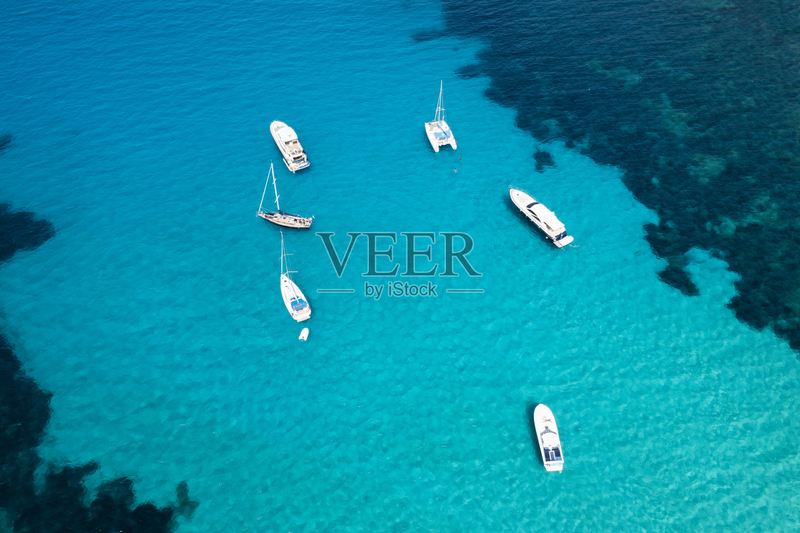 在阳光明媚的日子里,从空中俯瞰,一些船只和豪华游艇漂浮在蓝绿色、晶莹剔透的水面上,令人惊叹。意大利撒丁岛的翡翠海岸。照片摄影图片