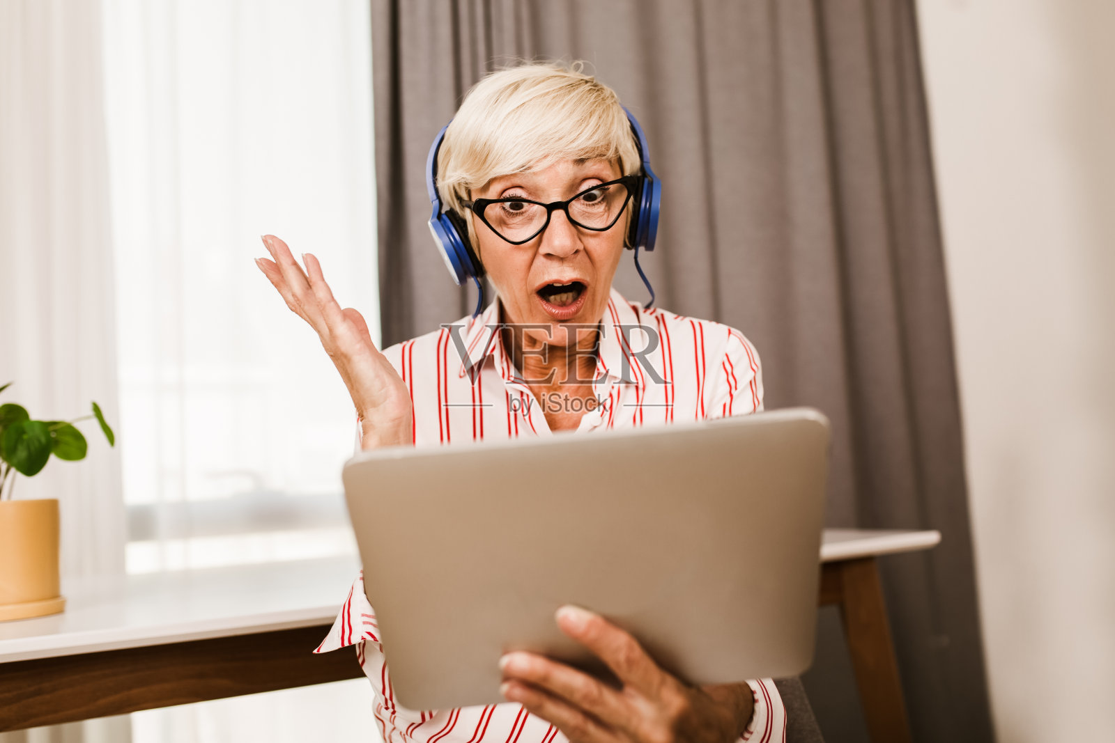 一个快乐的成熟女人一边向别人挥手,一边在家里用电子平板电脑进行视频通话。照片摄影图片