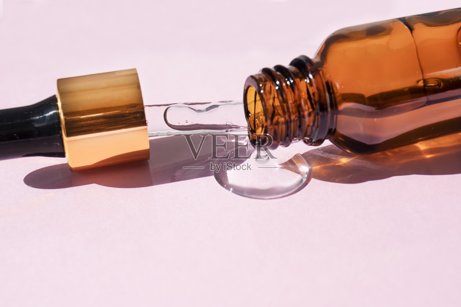 用棕色玻璃制成的滴管瓶在粉红色背景下投下阴影。从以上观点。照片摄影图片