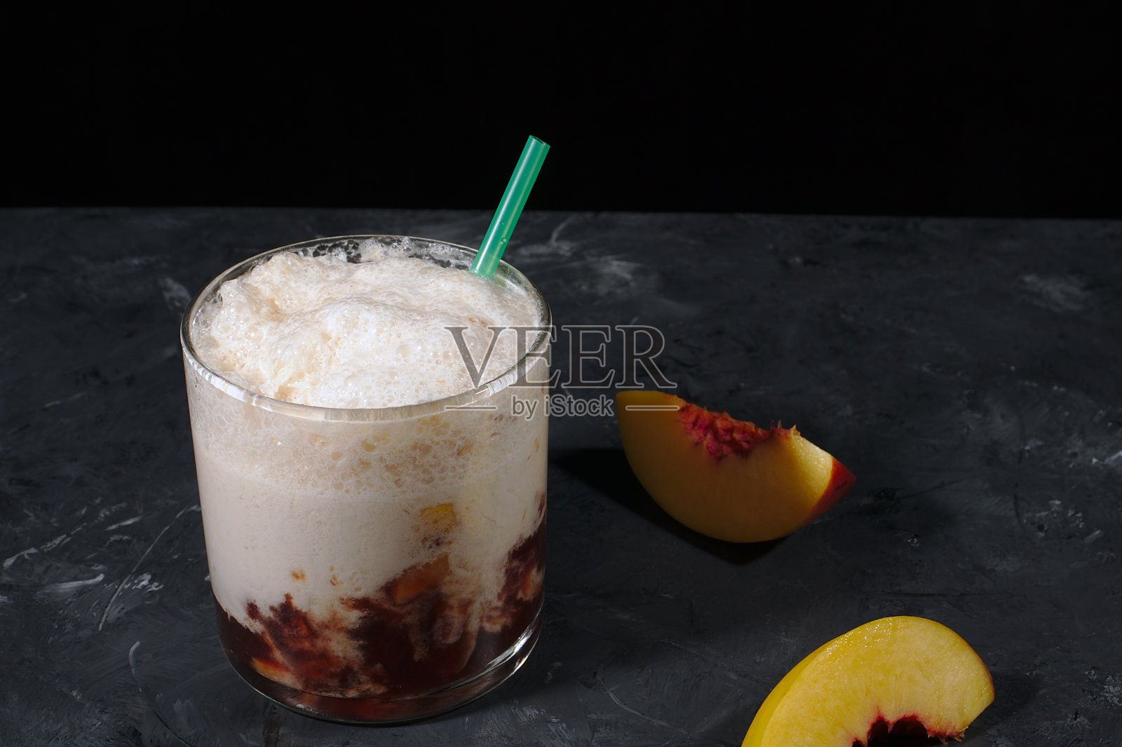 用新鲜油桃做成的奶昔放在桌上的玻璃杯里,黑色背景上是新鲜油桃片。照片摄影图片