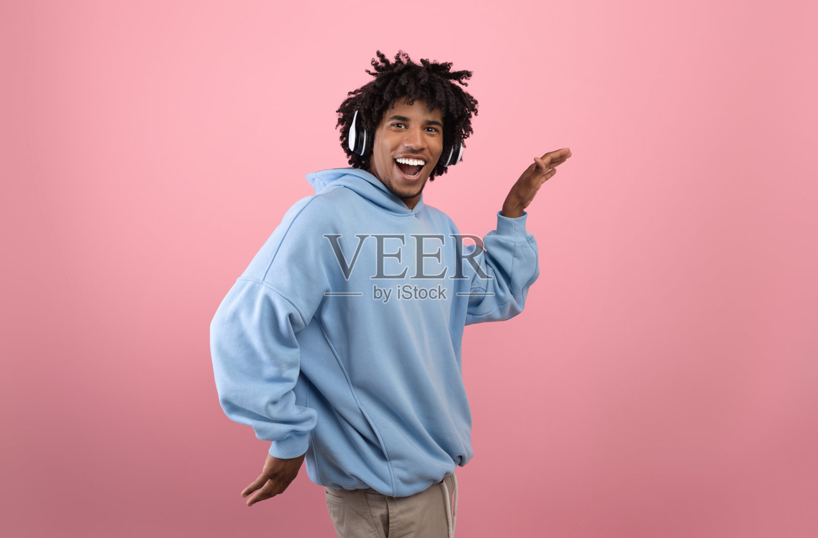 愚蠢的黑人少年戴着耳机听着音乐,跳着滑稽的埃及舞,在粉红色的背景上闲逛照片摄影图片