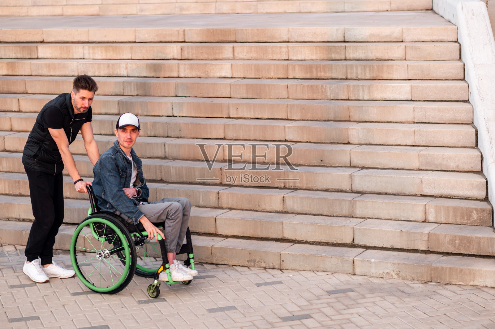 帮助有身体残疾的人。人驾驶轮椅,帮助他的朋友。人口社会服务。照片摄影图片