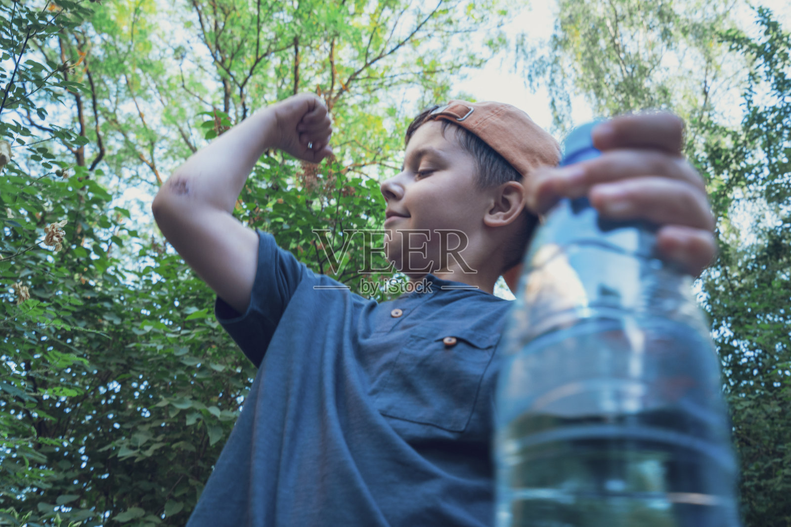 一个可爱的男孩拿着一瓶干净的水,展示他的二头肌照片摄影图片