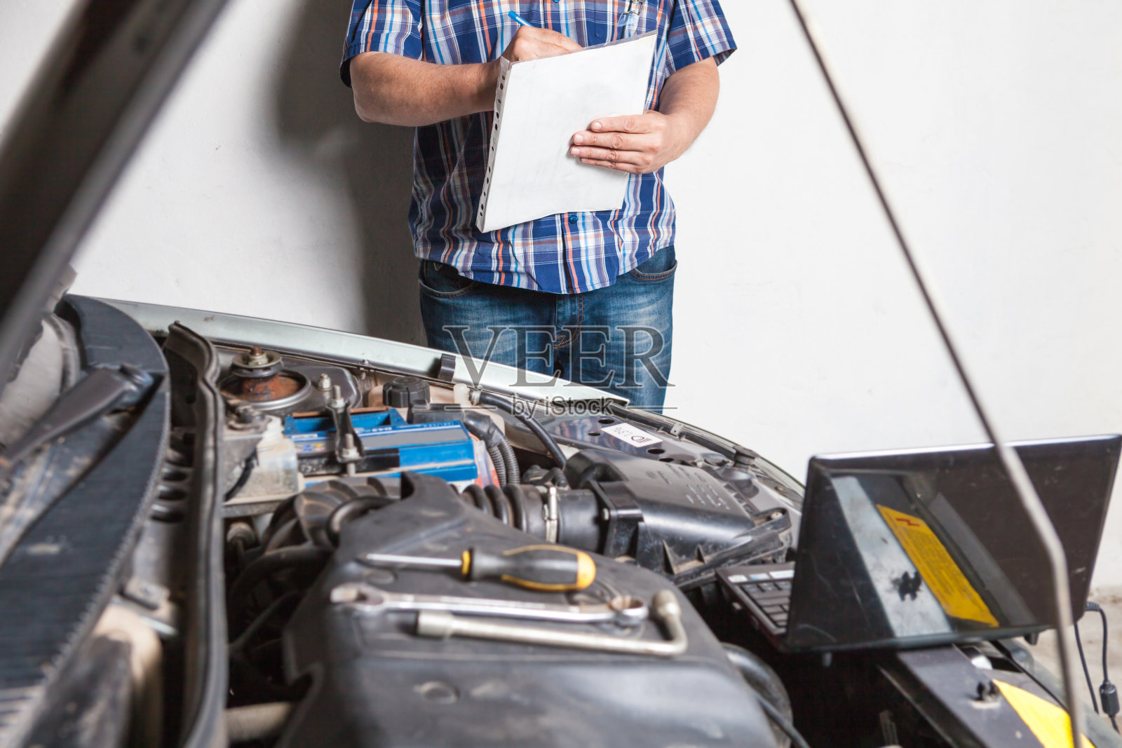 汽车技师拿着扳手在车库里修理汽车。照片摄影图片