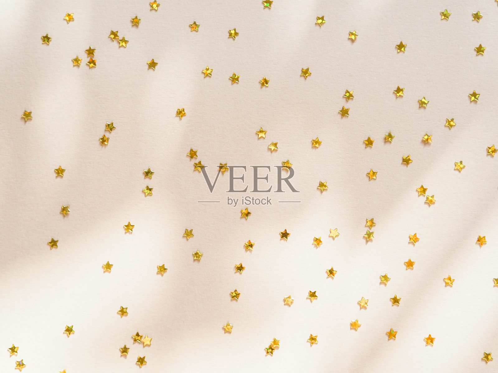 金色的星星以五彩纸屑的形式出现在米色的背景上照片摄影图片