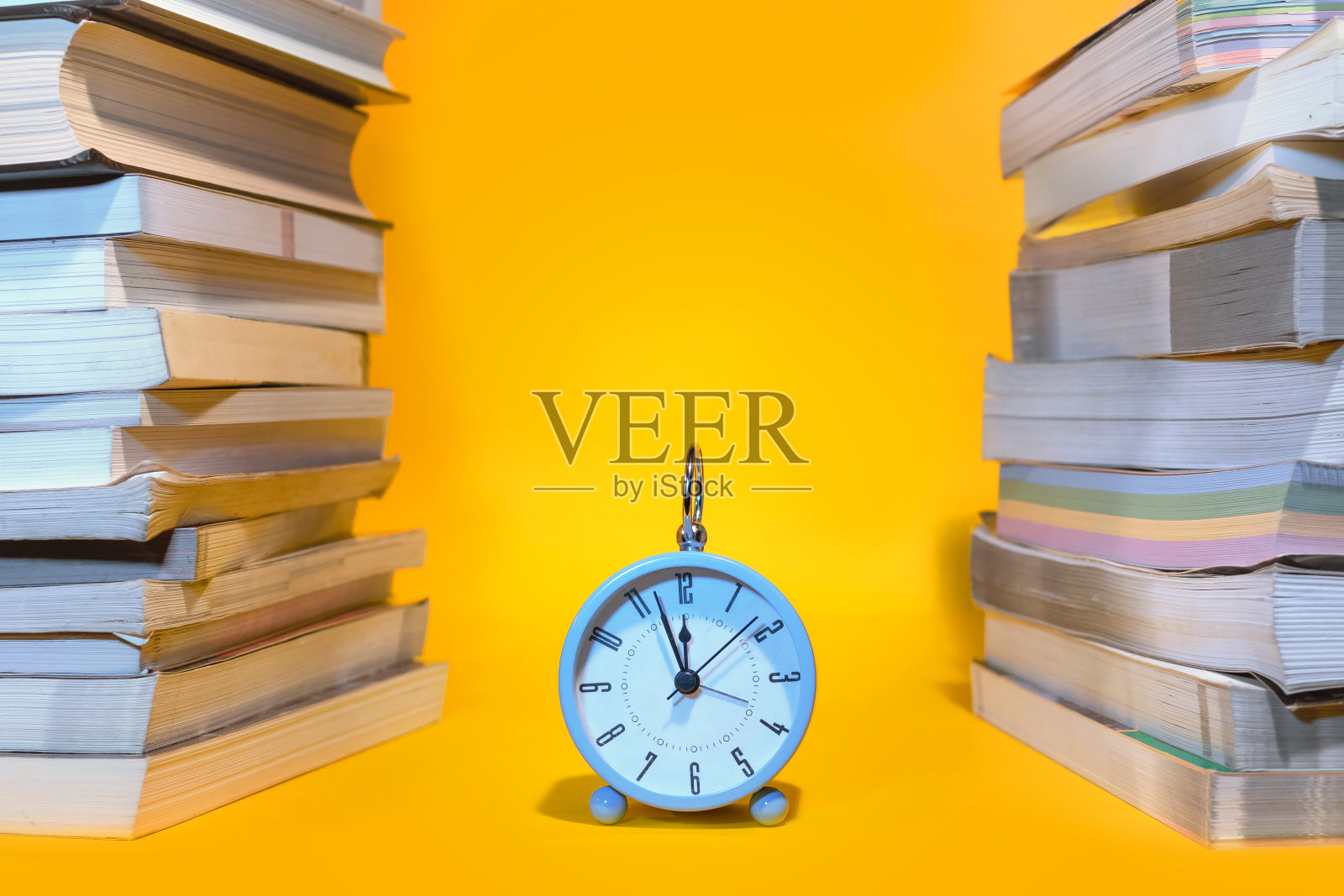 蓝色的闹钟和橙色背景下的一堆书照片摄影图片