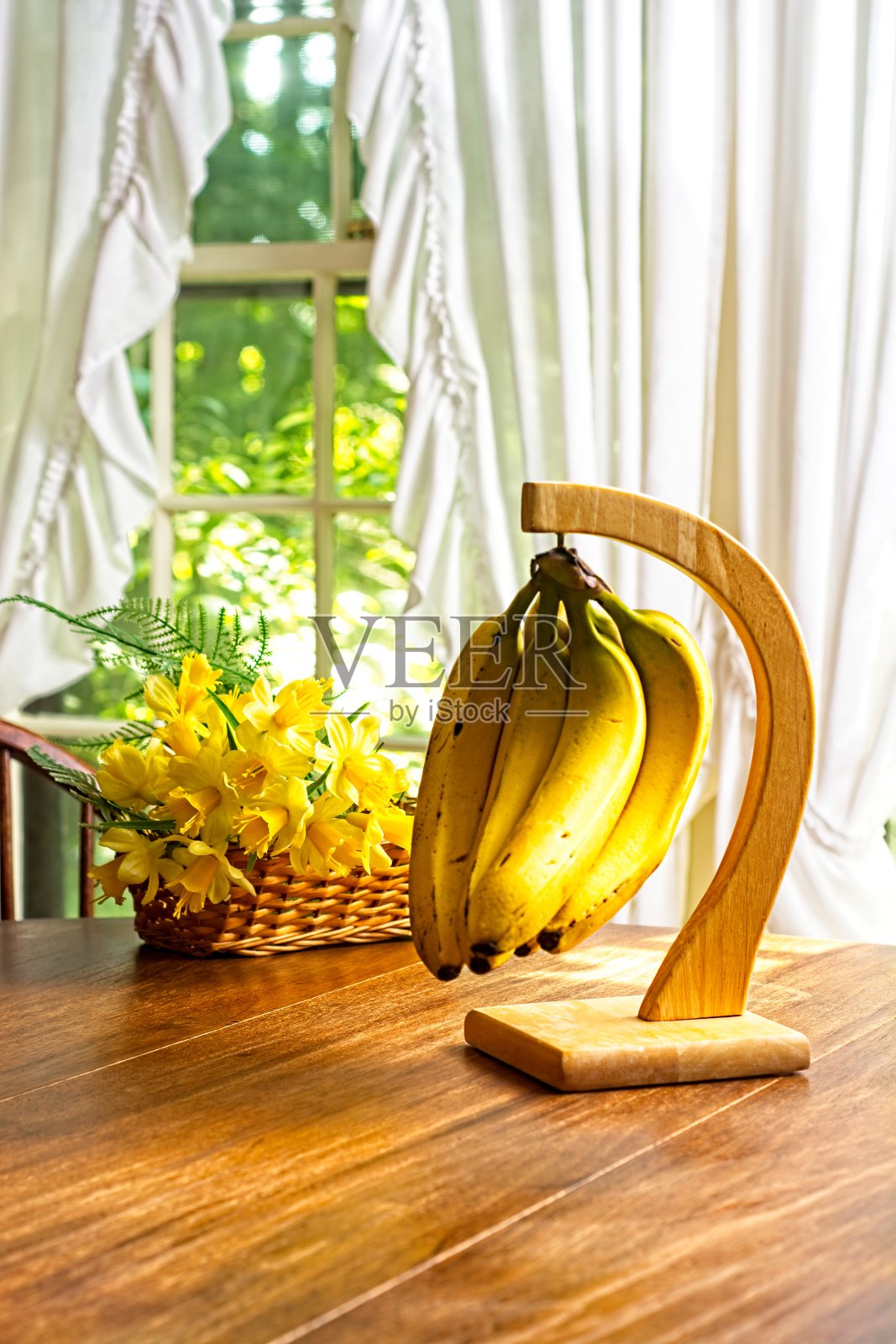 香蕉树放在阳光浸透的木制厨房桌子上,柳条篮子里装满了琼基尔花照片摄影图片