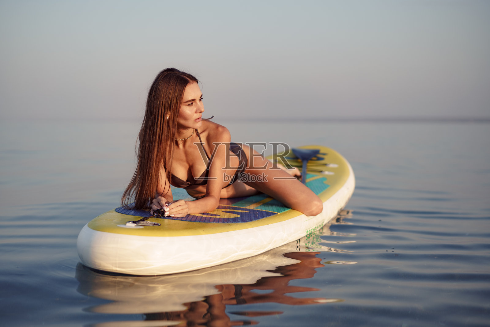 年轻的女人与性感的身体姿势在桨板在海照片摄影图片