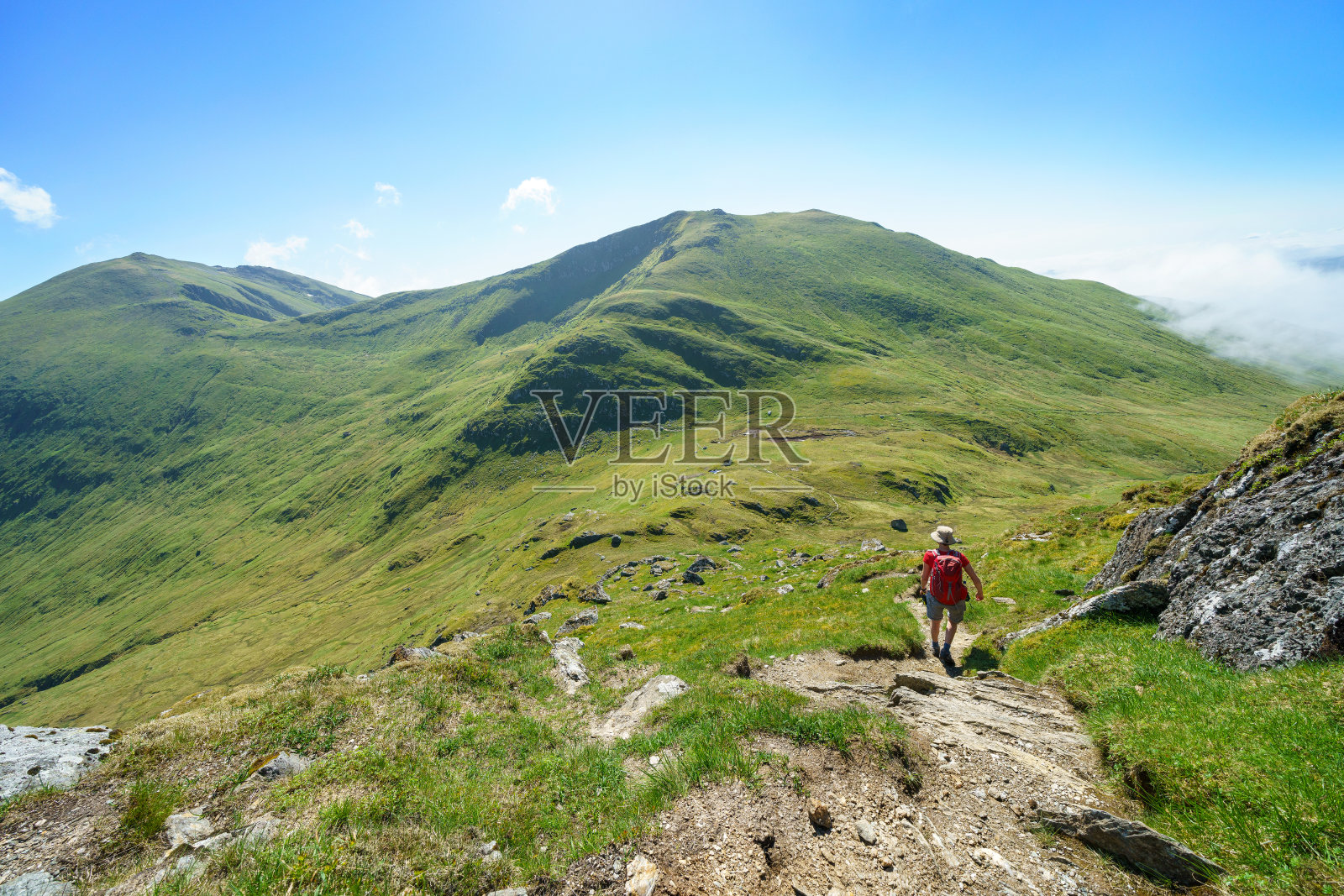 一名女性徒步旅行者和他们的狗从Meall Corranaich山顶走下来照片摄影图片