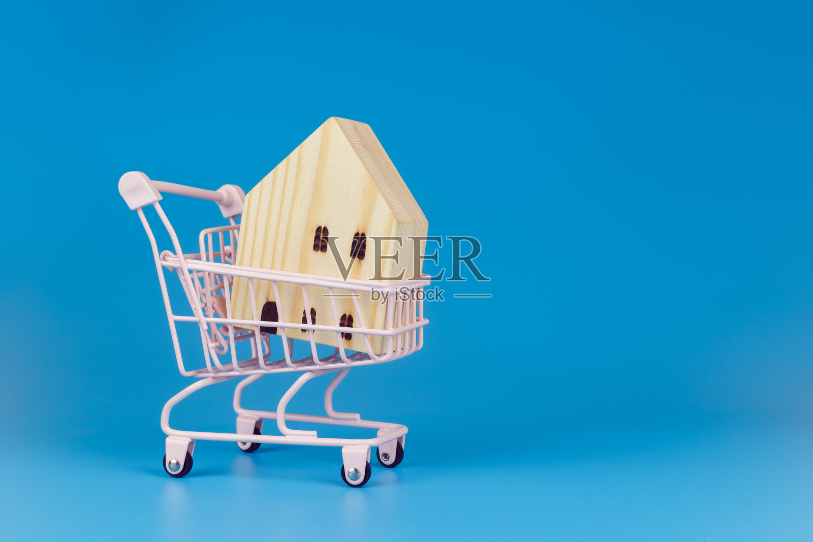 购物车与木制房子的蓝色背景,商业销售和购买的物业概念。照片摄影图片