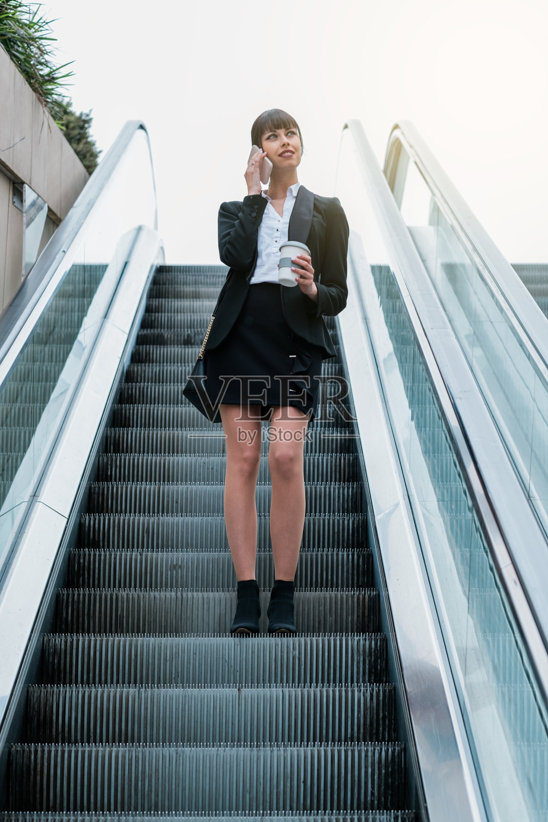 美丽的商业女性在自动扶梯上使用智能手机上班照片摄影图片