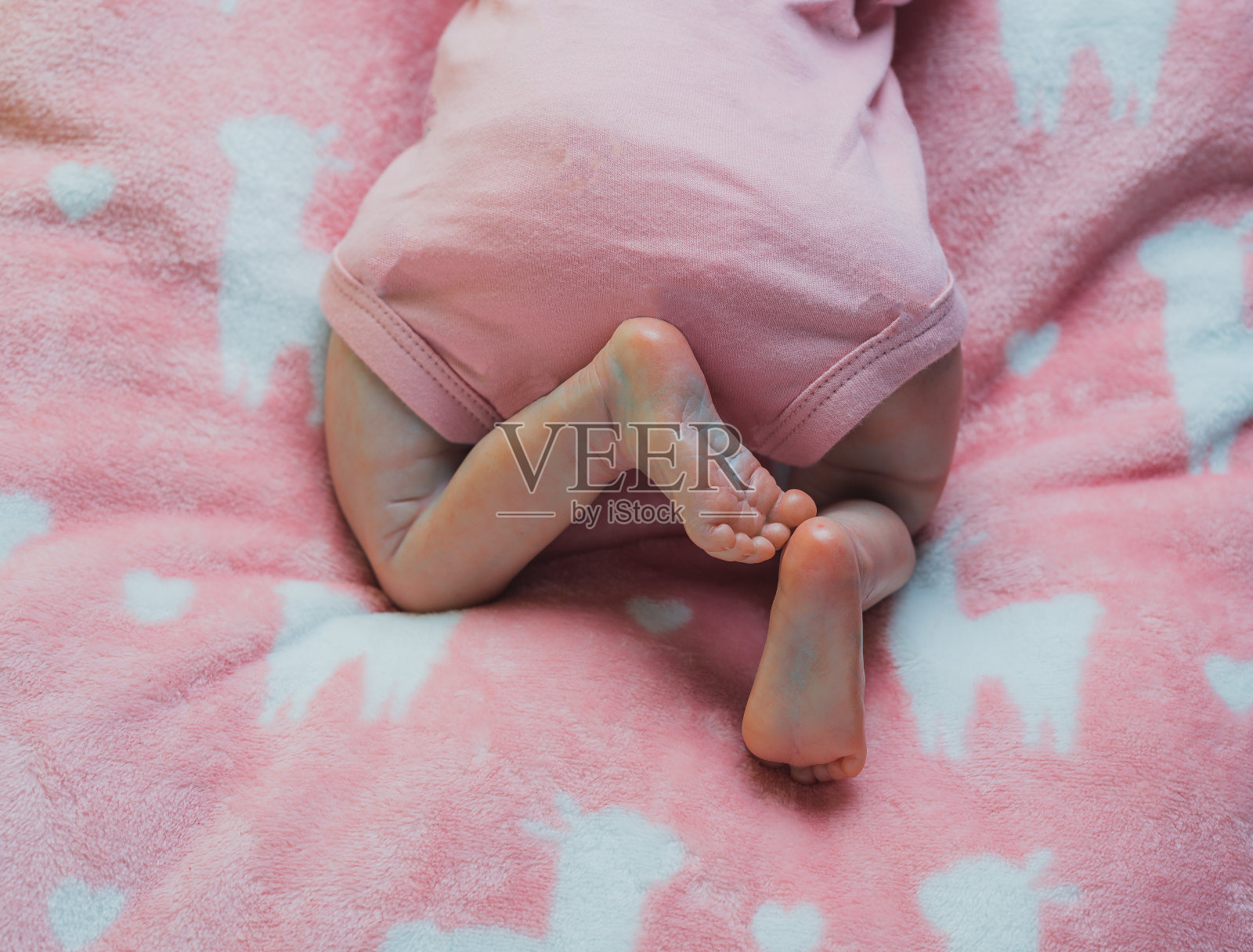 一个新生婴儿的腿,膝盖和脚的细节,在婴儿床里,穿着粉红色的衣服照片摄影图片