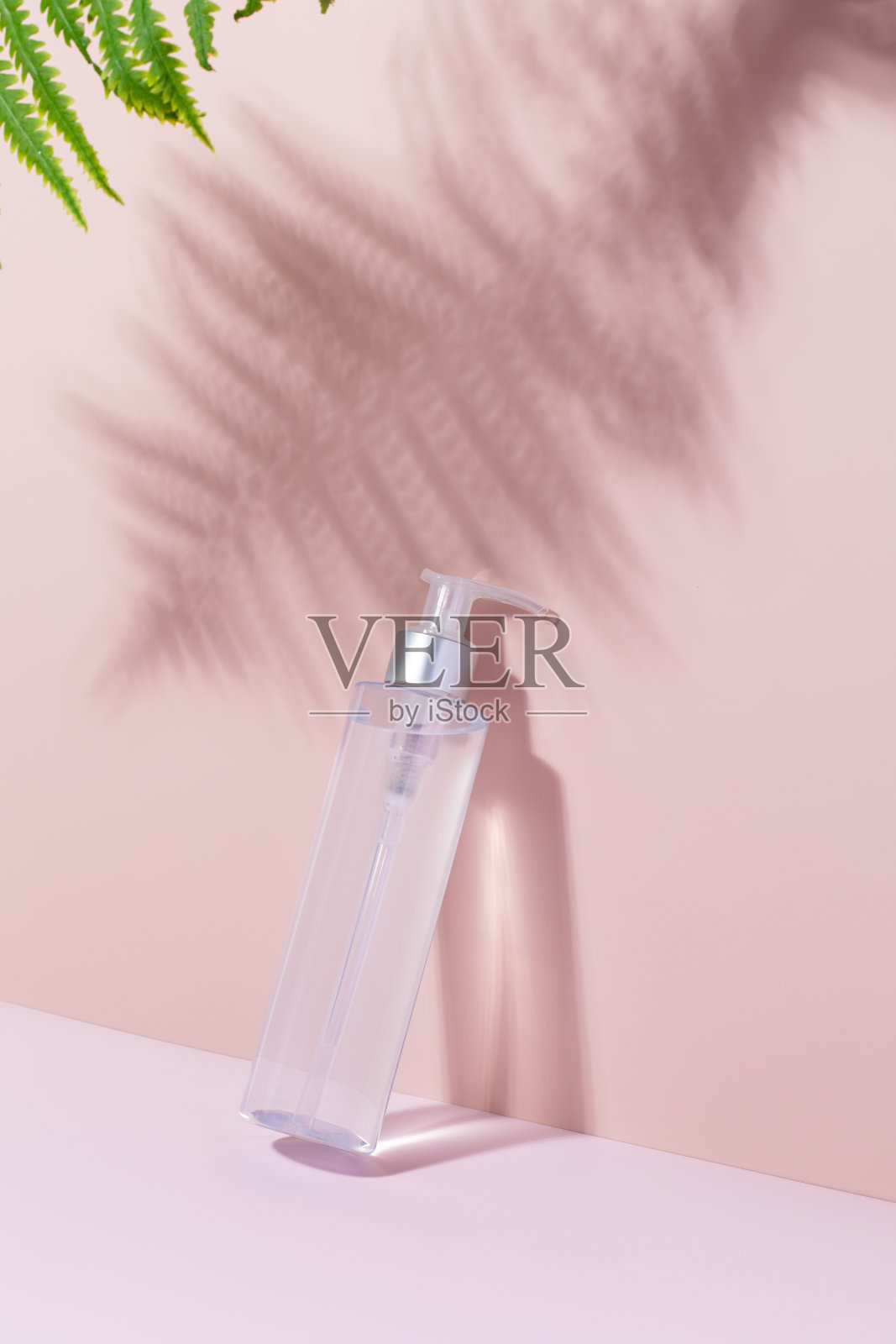 粉红色背景上有蕨类植物阴影的化妆品模型。洁面化妆水,胶束水。照片摄影图片