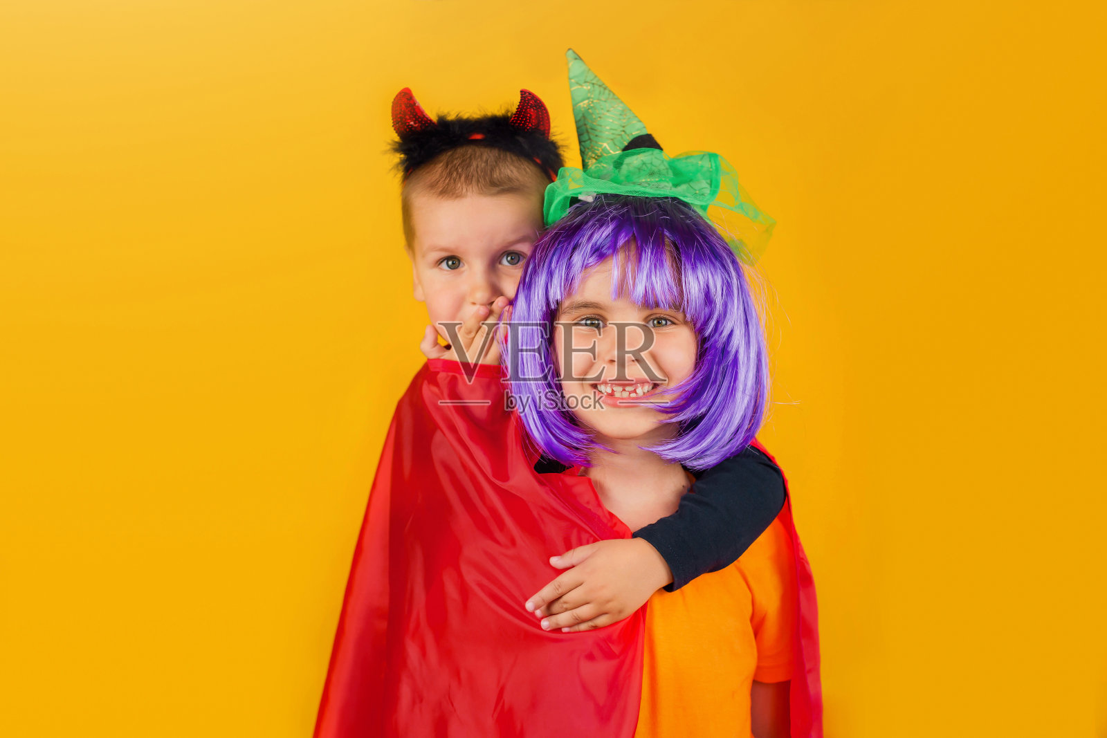 一个蹒跚学步的小男孩和小女孩穿着万圣节的狂欢节服装被孤立在黄色背景上。传统节日的概念。照片摄影图片