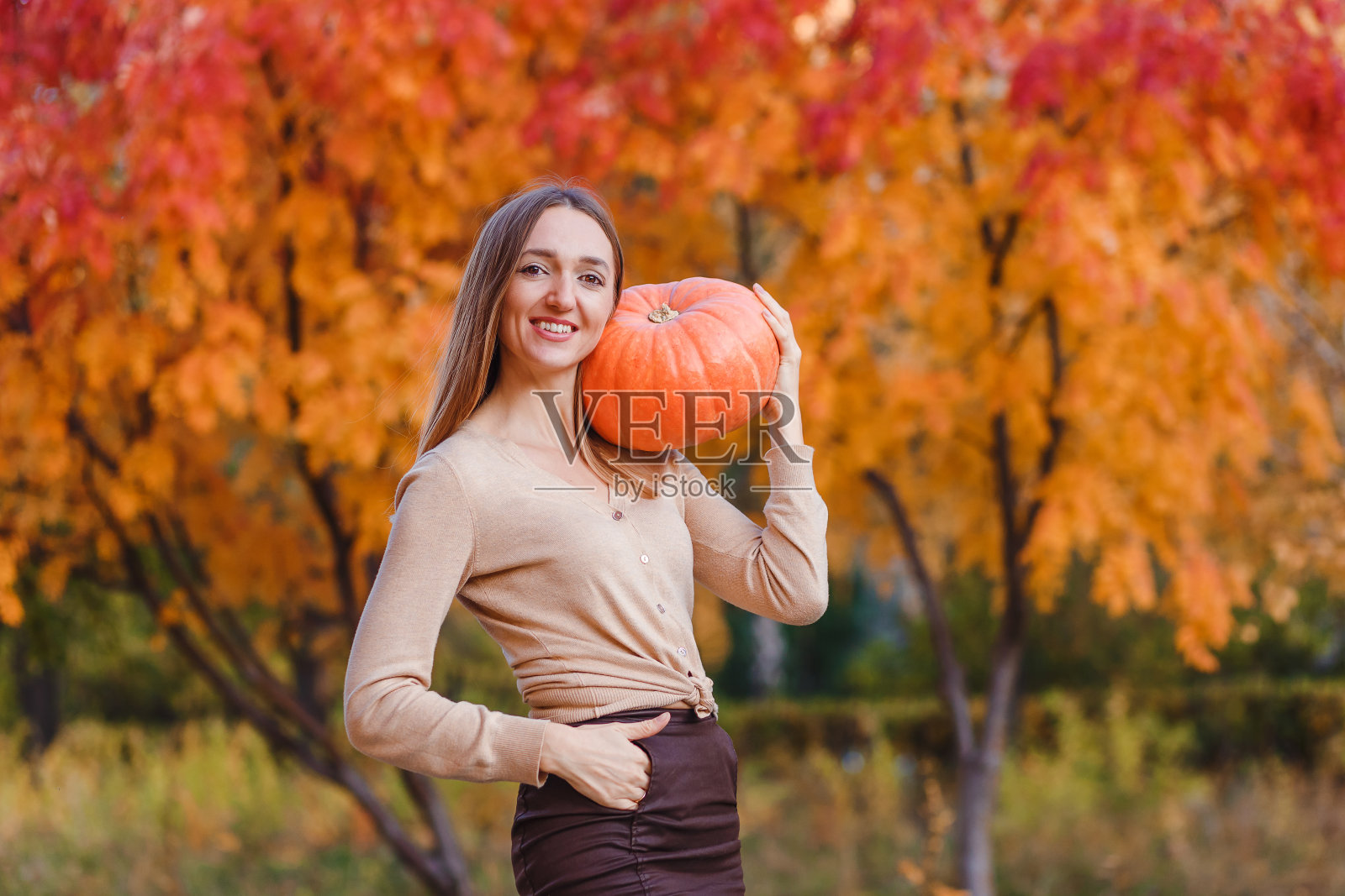 30岁的欧洲妇女微笑着拿着一个美丽的橙色南瓜,背景是模糊的美丽的自然照片摄影图片