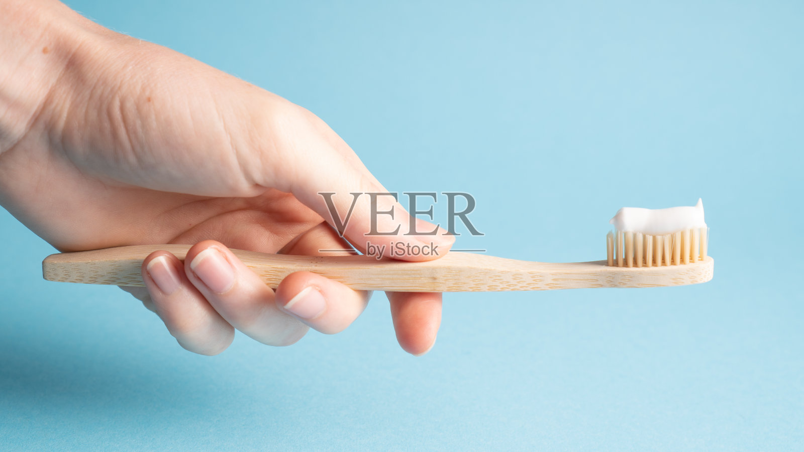 手里拿着蓝色的竹牙刷。手持木质环保牙刷。竹牙刷上的天然牙膏照片摄影图片