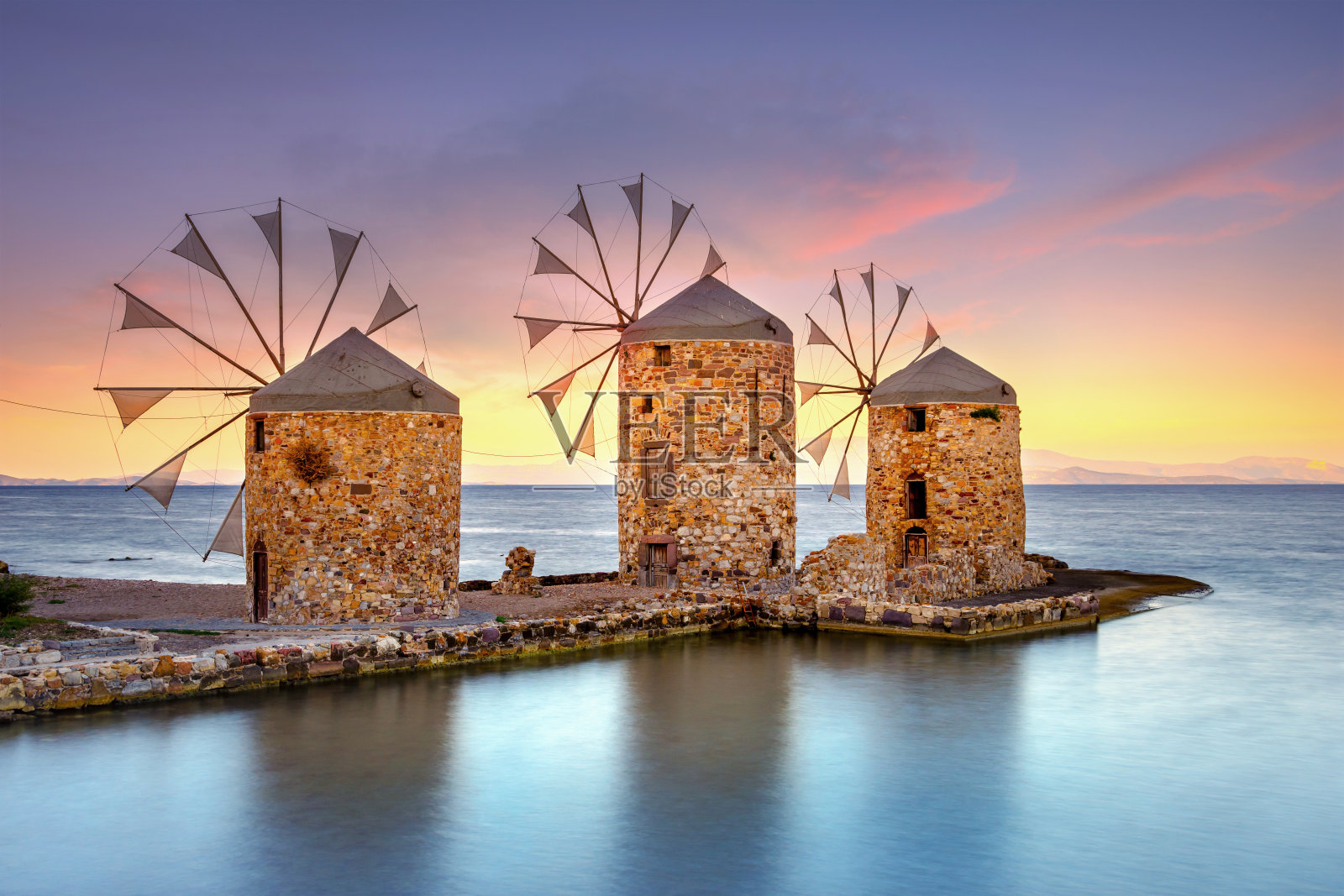 希腊希奥斯岛海滩上的老风车。照片摄影图片