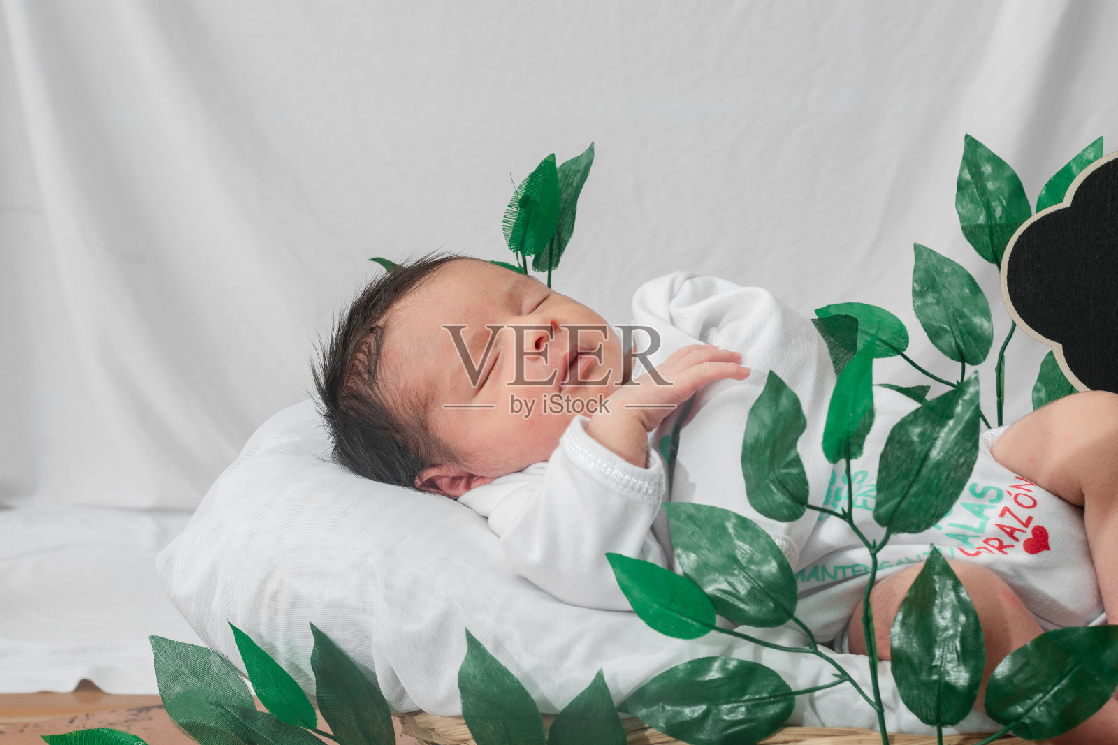 美丽的新生婴儿(4天大)侧睡在竹纤维篮子里,被绿叶环绕,健康的医疗理念照片摄影图片