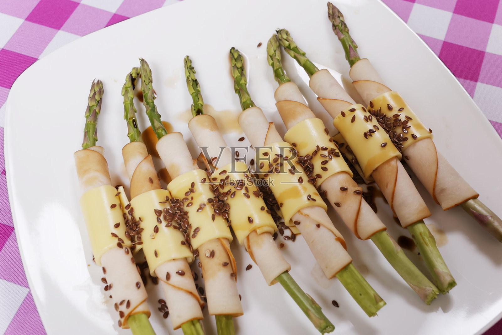 烤芦笋包裹火腿,奶酪,亚麻籽和酱油,紫色,黄色和蓝色的格子桌布为背景。照片摄影图片