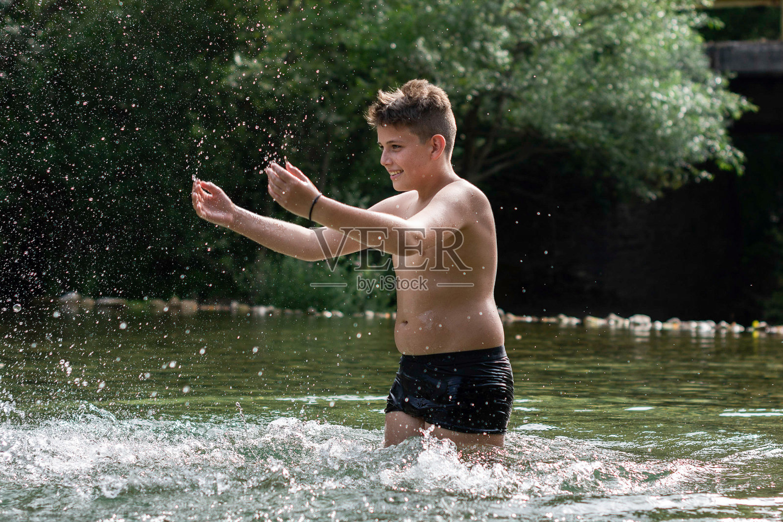 男孩在河里泼水照片摄影图片