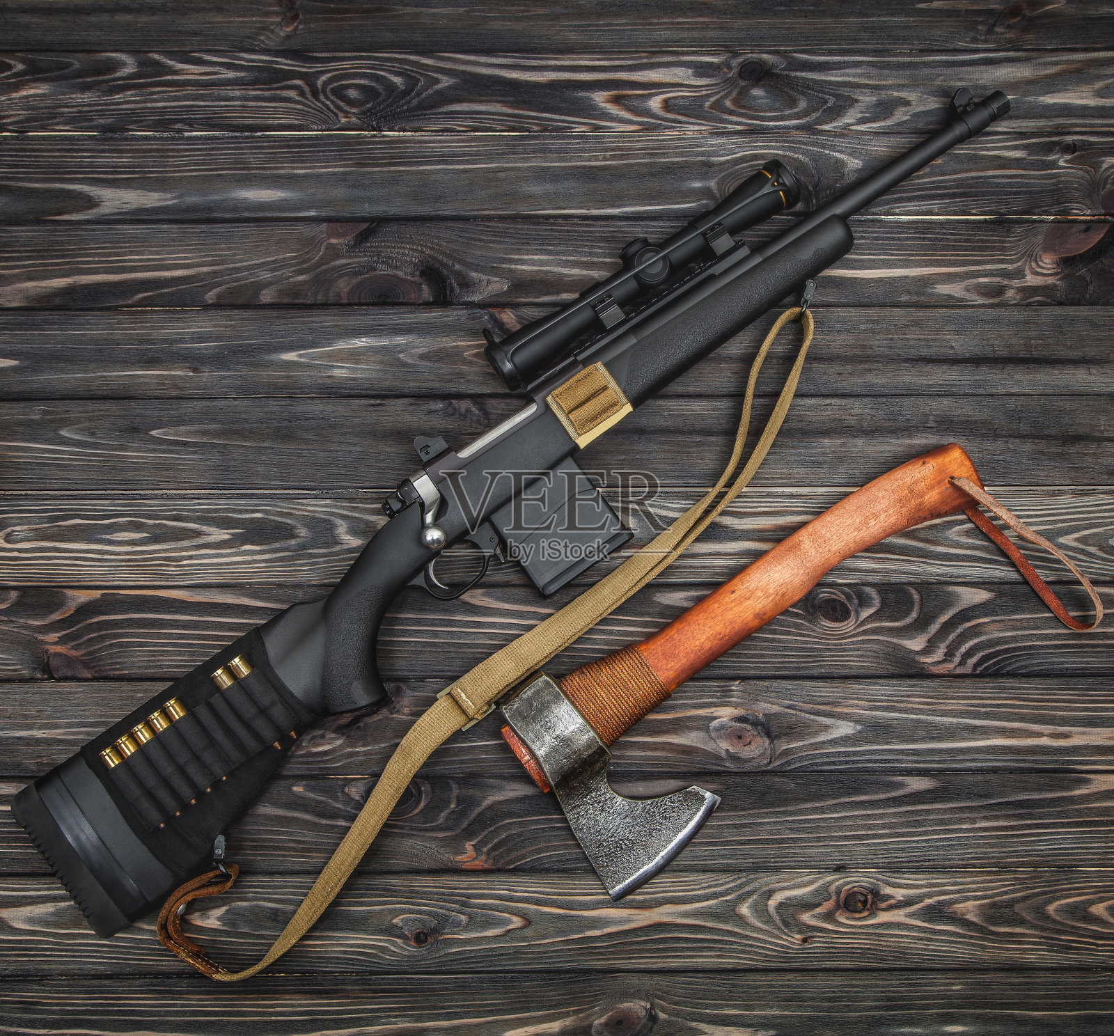 一块木板上放着一把现代的螺栓式步枪,配有望远镜瞄准器和一把木柄斧头。男人的集合。猎人侦察装备。木制背景上的生存武器。照片摄影图片