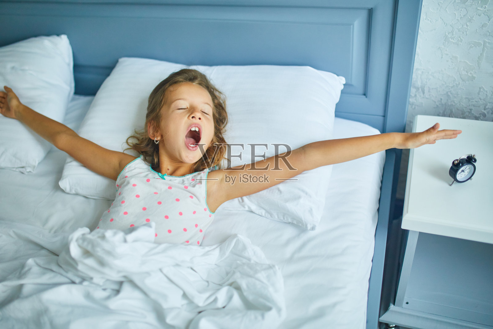 小女孩从家里一张又大又舒适的床上醒来,床上有白色的亚麻布照片摄影图片