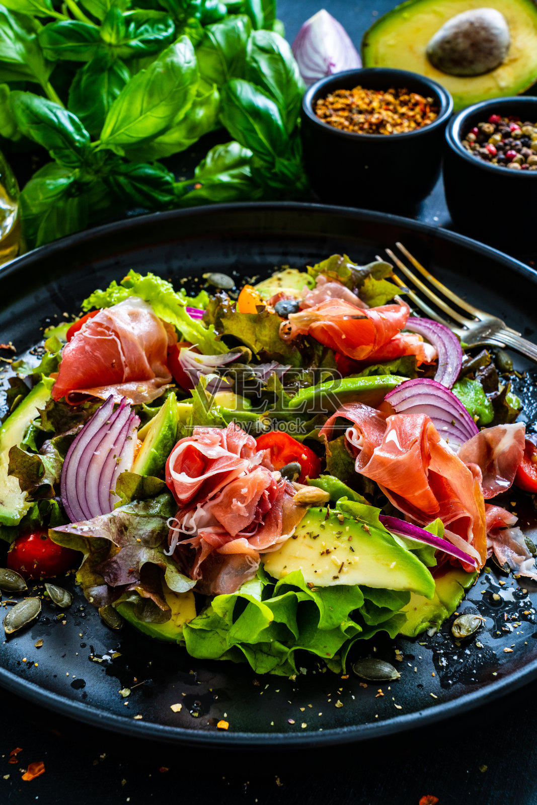 美味的沙拉-帕尔马火腿,鳄梨,迷你番茄和新鲜的绿色蔬菜木制背景照片摄影图片