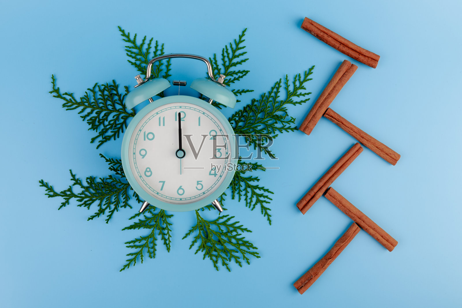 闹钟,柏树树枝和肉桂棒在蓝色背景。圣诞节的概念。照片摄影图片