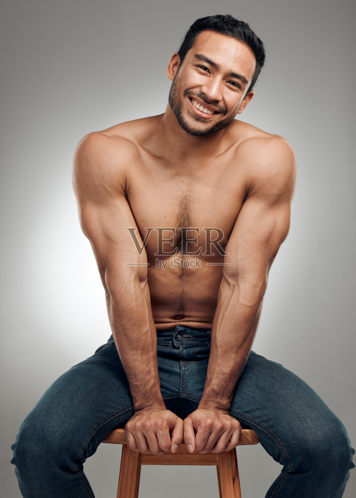 一个英俊的年轻人坐在工作室的凳子上,摆出赤裸的姿势照片摄影图片