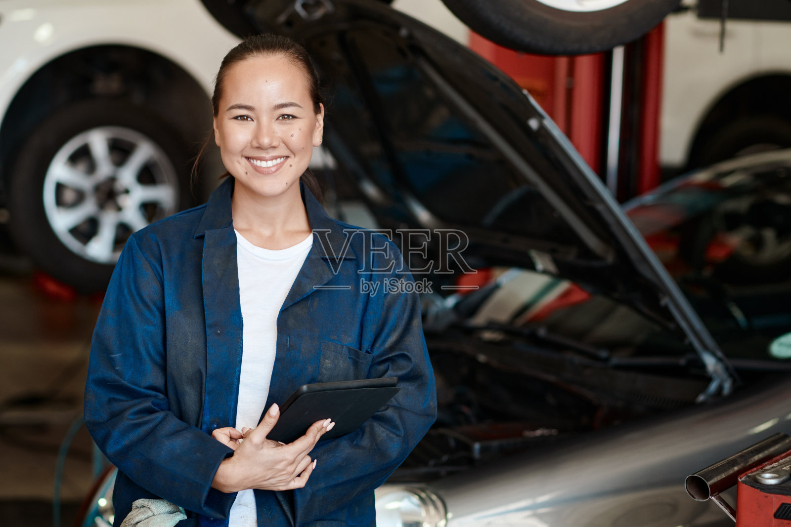 图为一名女机械师在汽车修理店工作时,手拿数码平板电脑照片摄影图片