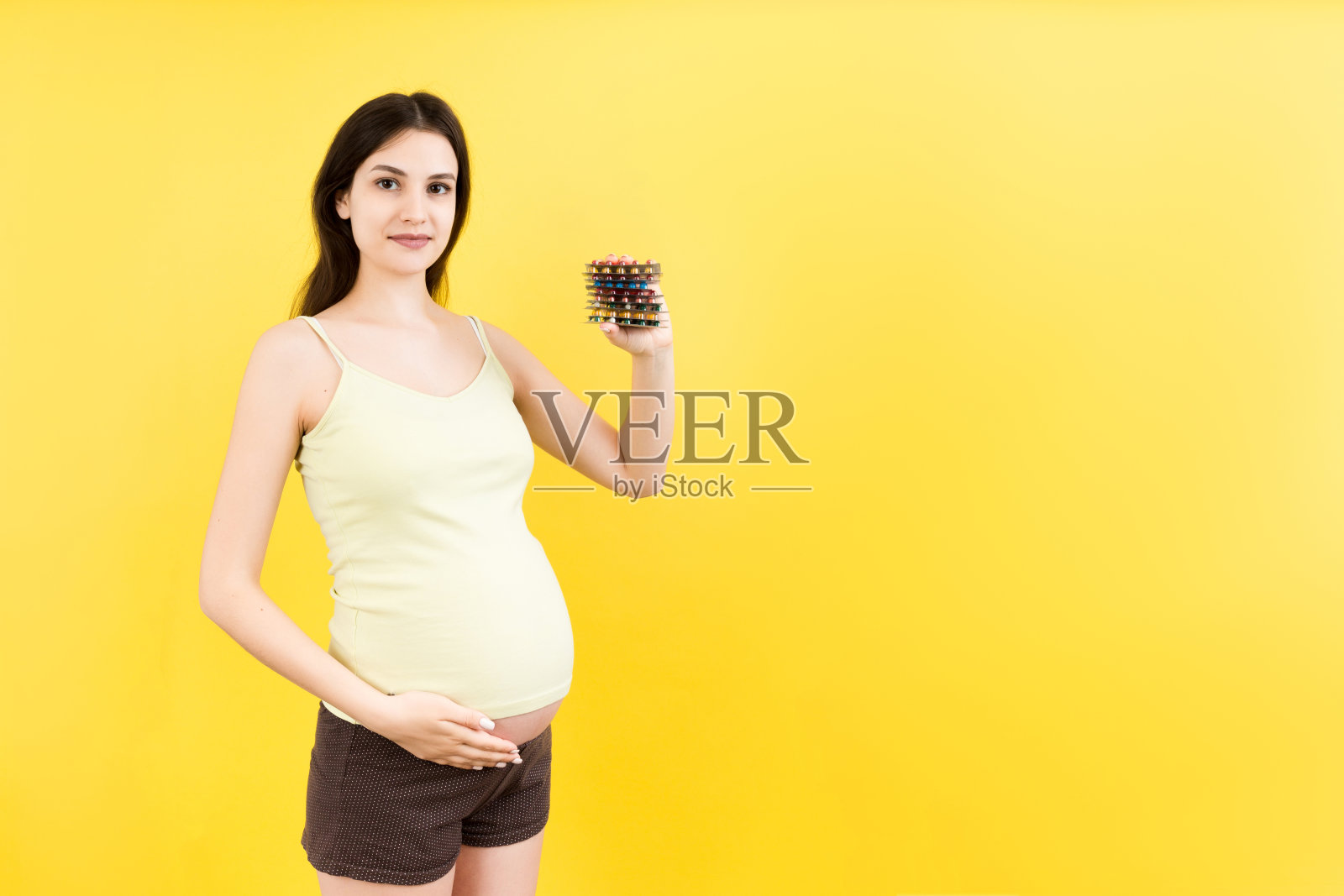 成堆的水泡药丸在孕妇的手在彩色的背景与复制空间。怀孕期间的保健和治疗照片摄影图片