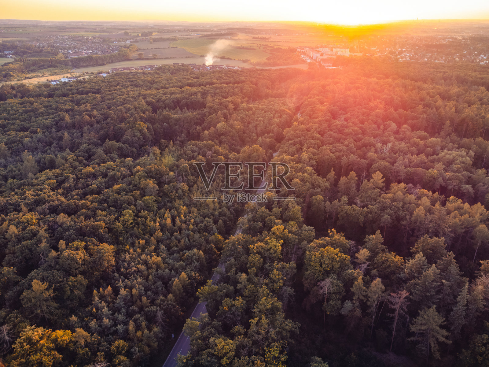 从空中到地面的视野。森林里的路。从一架无人机上,日落时分。那座城市可以在远处看到。照片摄影图片