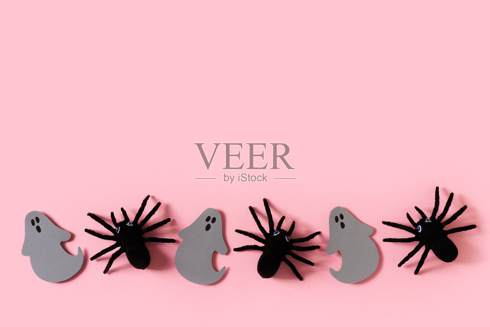 万圣节卡片上有黑色的蜘蛛,灰色的幽灵和粉红色背景上的五彩纸屑照片摄影图片