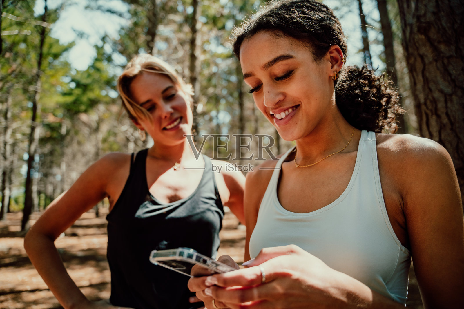 两个女性朋友一起站在森林里,微笑着用手机发短信照片摄影图片