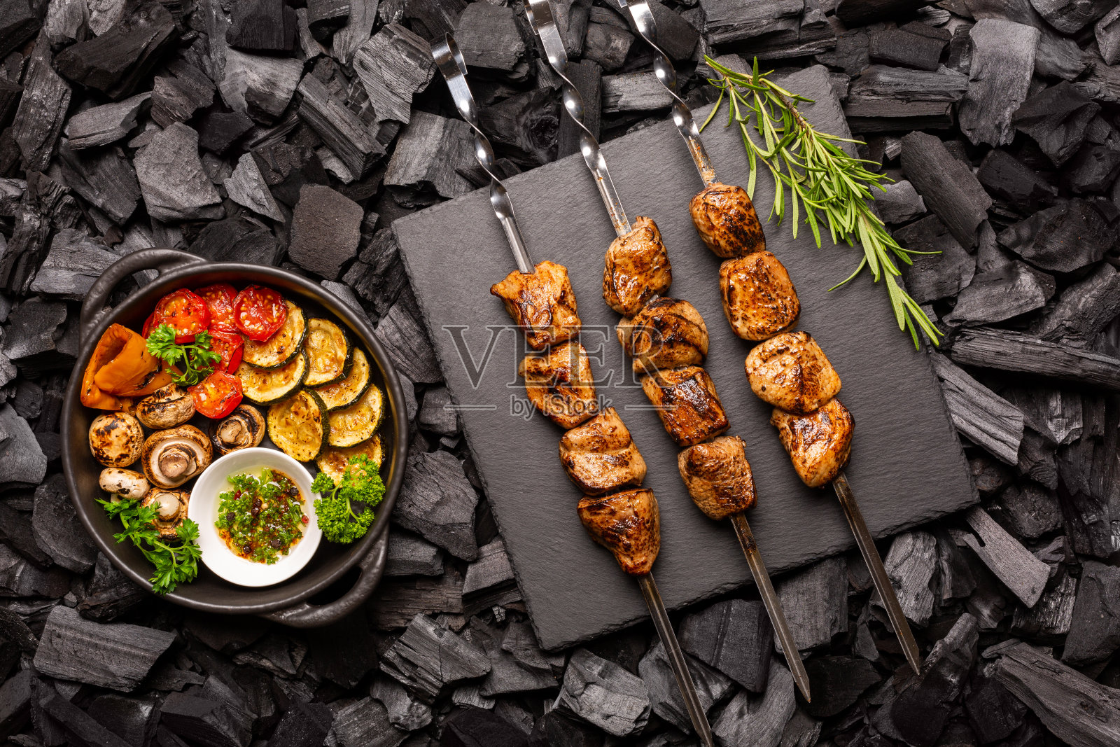 自制的烤肉串放在石头砧板上,烧烤蔬菜放在煤煎锅里。前视图。照片摄影图片