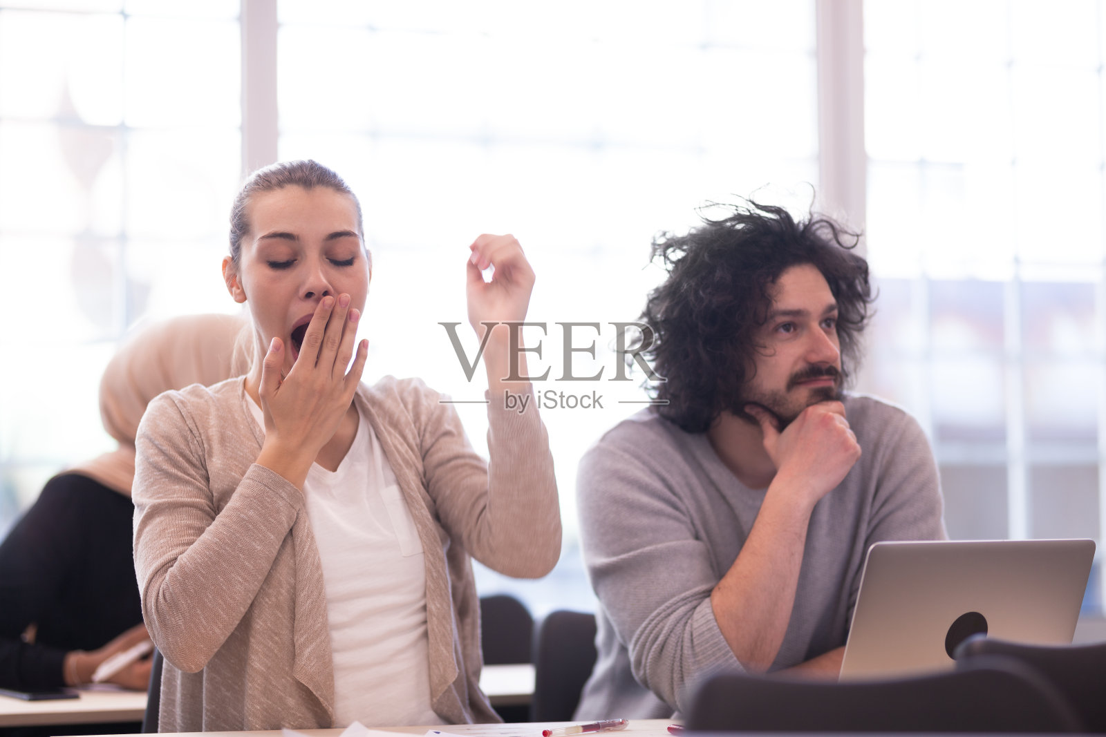 学生们在教室里听老师讲课。聪明的年轻女孩在上课时打哈欠。照片摄影图片