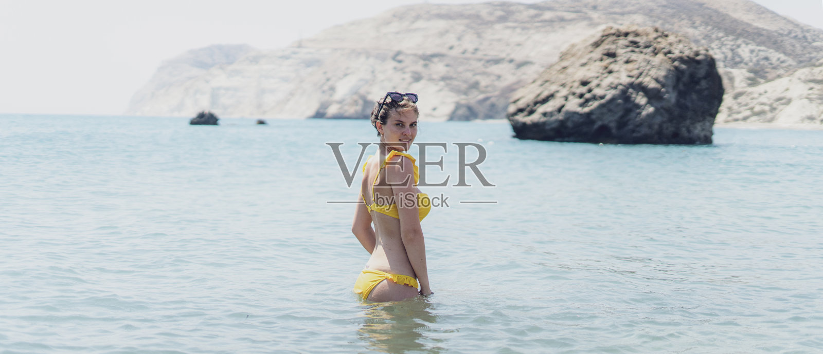 年轻的女孩站在夏日海滩的海水里,从后面看照片摄影图片