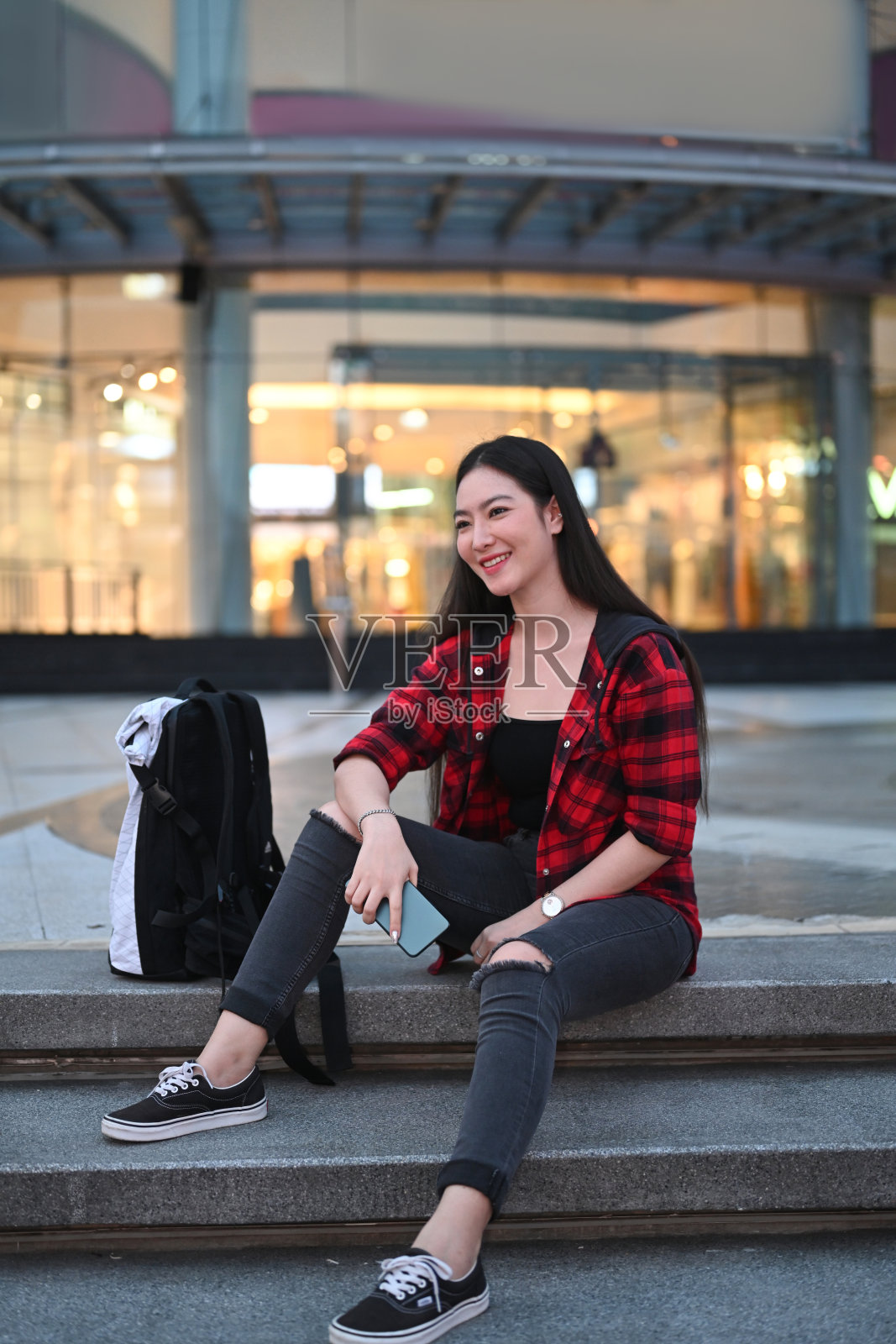 一个微笑的年轻女子坐在商场的楼梯上。照片摄影图片