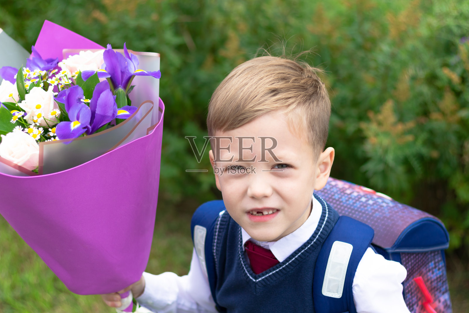 9月1日假期结束后,一名可爱的一年级男孩穿着校服,手捧一束五颜六色的鲜花在校园里。知识的一天照片摄影图片
