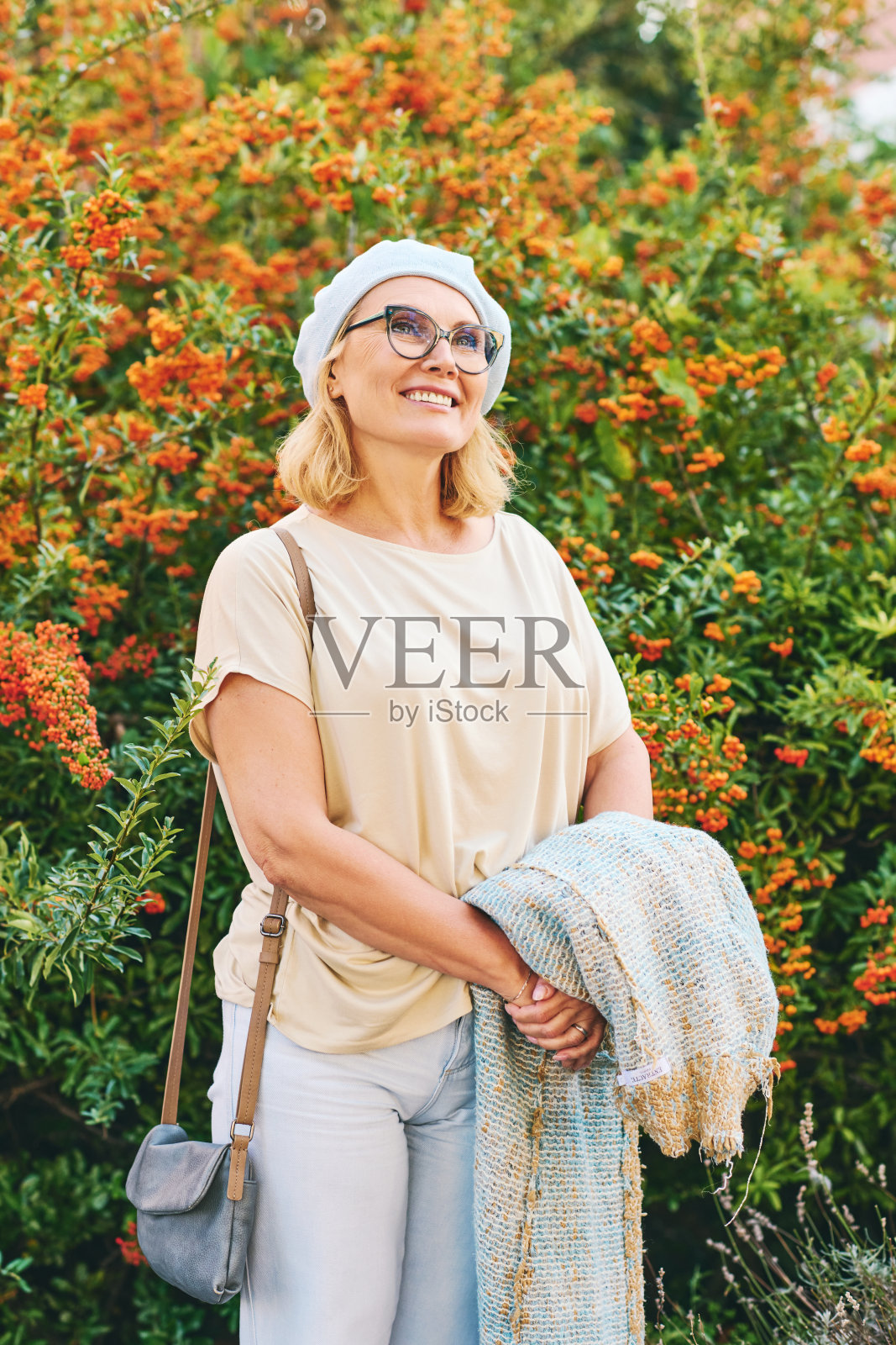 快乐的中年妇女在明亮的桔红色火刺浆果旁摆姿势的户外肖像照片摄影图片