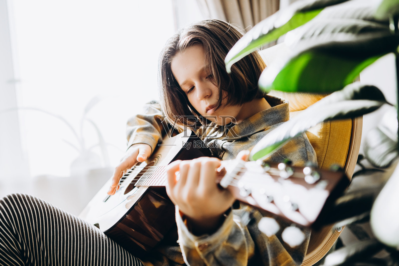 十几岁的女孩坐在家里的椅子上弹吉他。在线吉他培训。我的爱好是检疫照片摄影图片