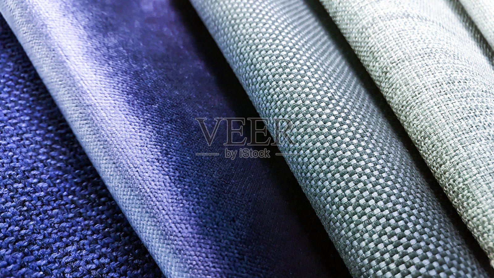 窗帘或窗帘织物的样品。生产用于家具装饰的软垫、细部。微距视图照片,选择性聚焦在灰色织物纹理。灰色和蓝色天鹅绒面料样品。照片摄影图片