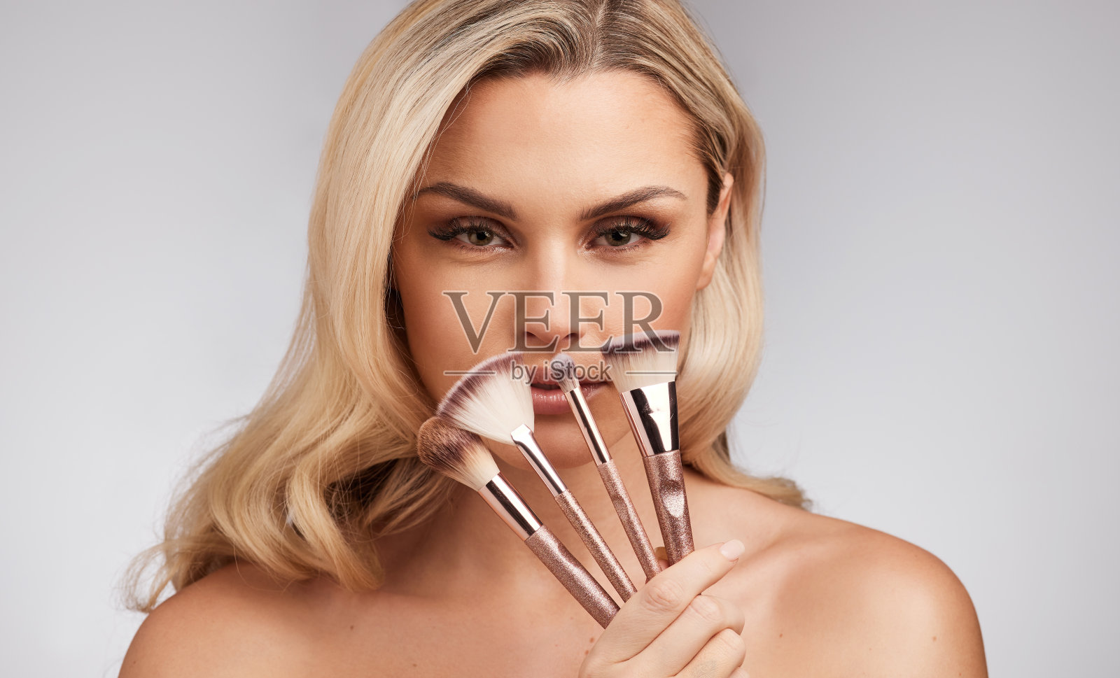 一个美丽的年轻女子拿着一套化妆刷在灰色背景的工作室肖像照片摄影图片