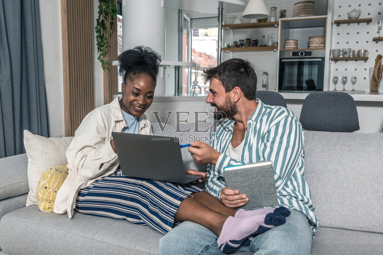 一对年轻幸福的夫妇,经营着一家新开的小公司,他们坐在家里。妻子用笔记本电脑监控网站上的统计数据,丈夫计算成本和利润照片摄影图片