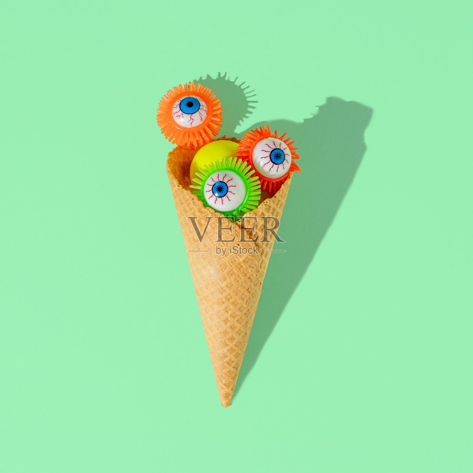 淡绿色背景上有彩色眼球的冰淇淋角。恐怖的万圣节食物概念。照片摄影图片
