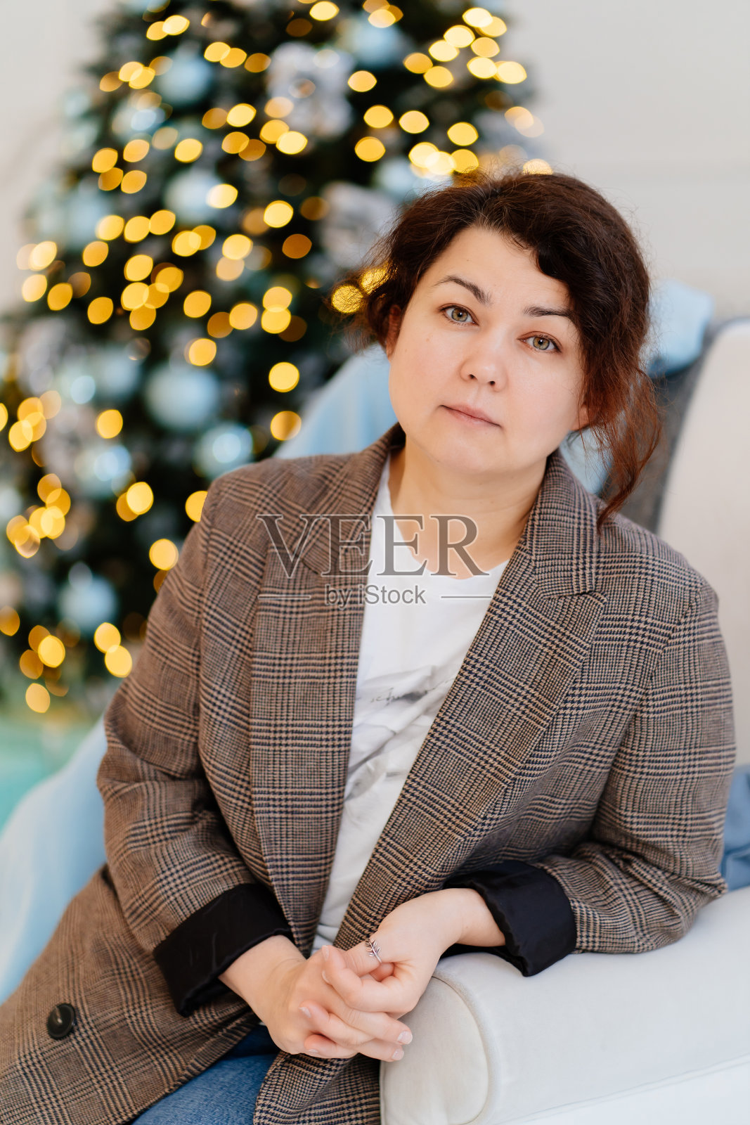 没有化妆的中年黑发女人站在圣诞树的背景下照片摄影图片