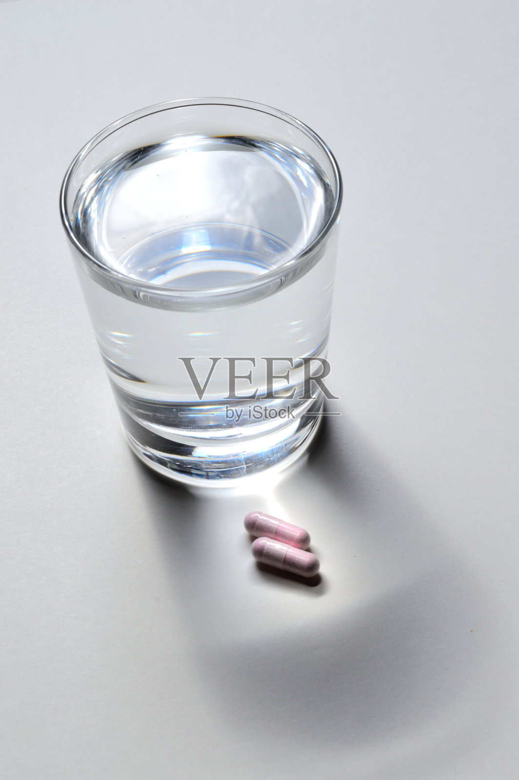 一个玻璃烧杯和两粒含有维生素的粉色胶囊。特写镜头照片摄影图片