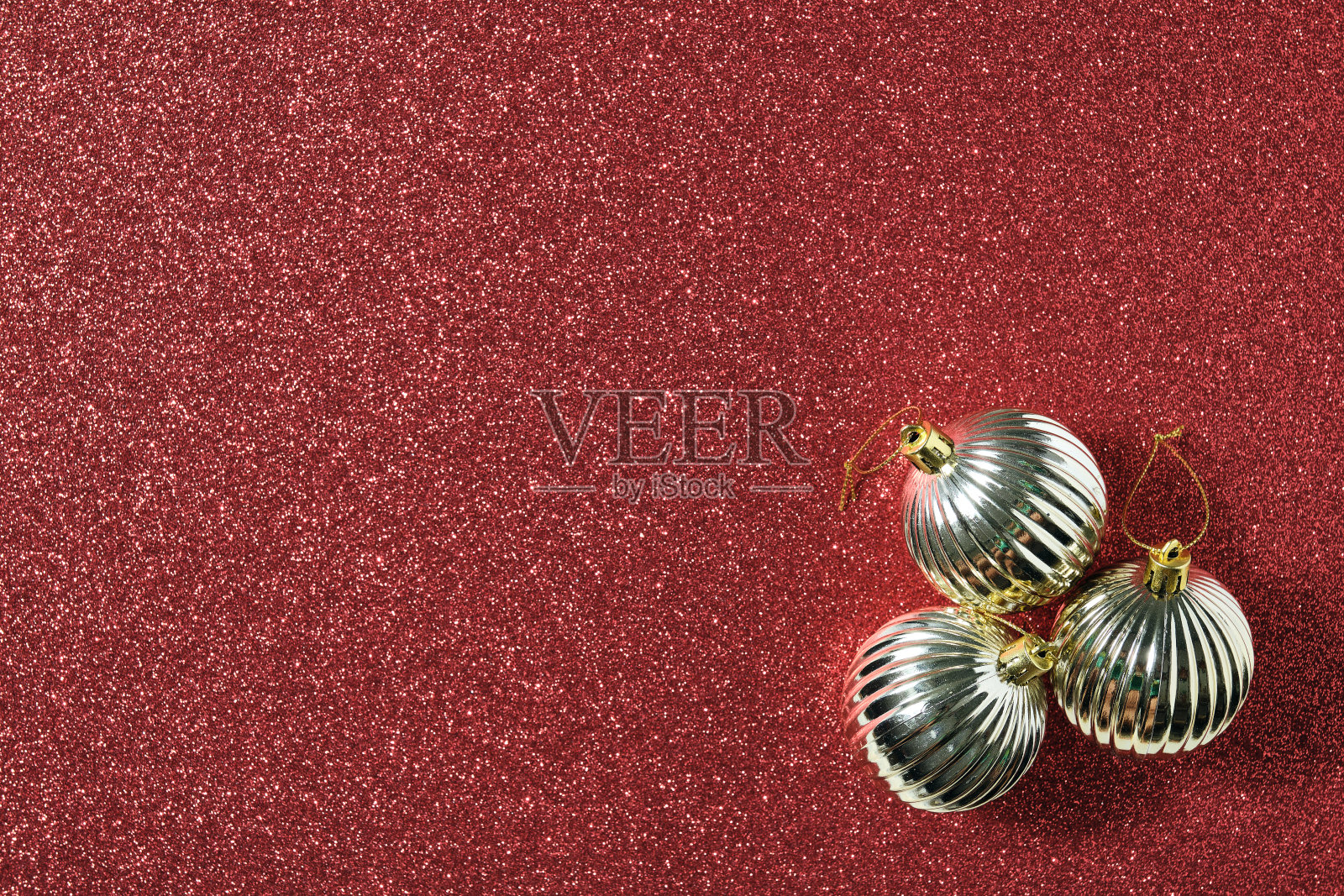 右下角的三个闪亮的金色圣诞球在闪亮的红色背景下照片摄影图片
